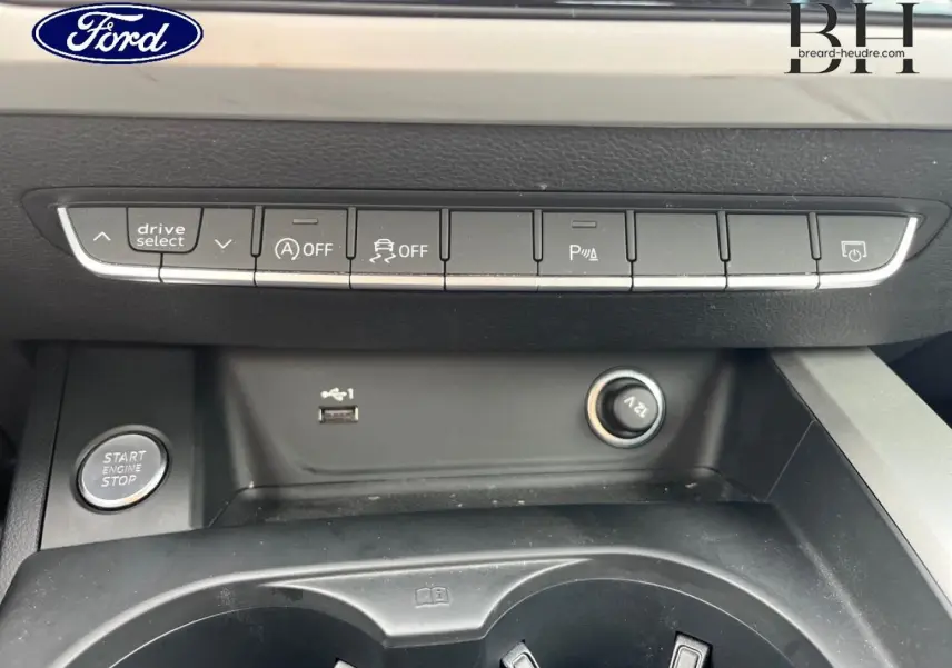 Vue rapprochée de la console centrale d'une Audi A4 Avant gris Manhattan, avec boutons de contrôle et prise 12V visibles.