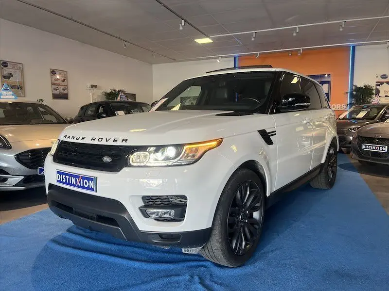 Range Rover Sport blanc vu en 3/4 avant droit dans un showroom avec jantes noires et calandre noire.