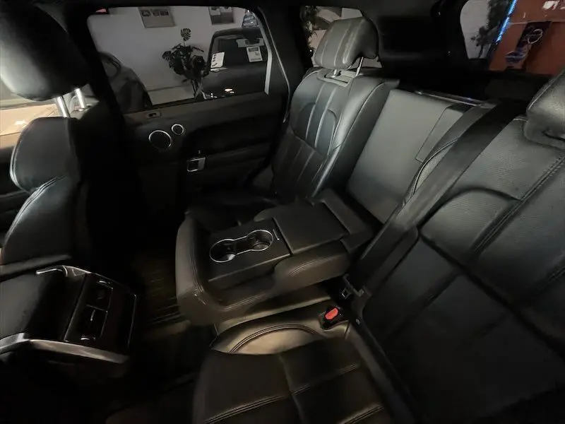 Vue intérieure arrière du Range Rover Sport blanc 2018, sièges en cuir noir avec accoudoir central et porte-gobelets intégrés.