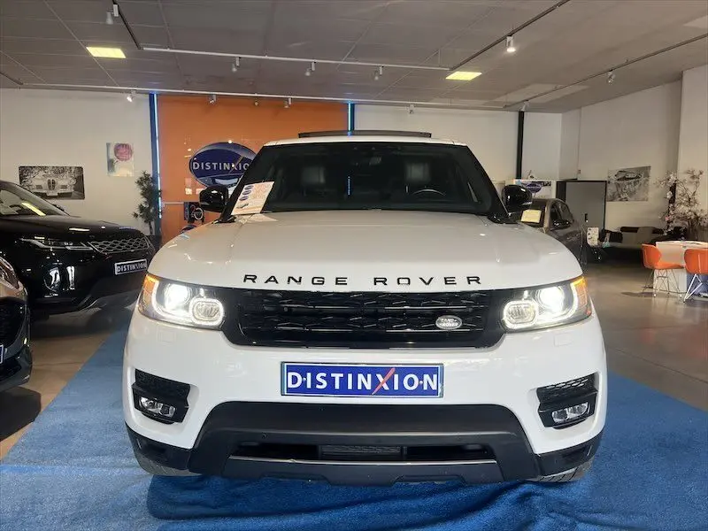 Vue frontale d'un Range Rover Sport blanc avec calandre noire et phares allumés dans un showroom.
