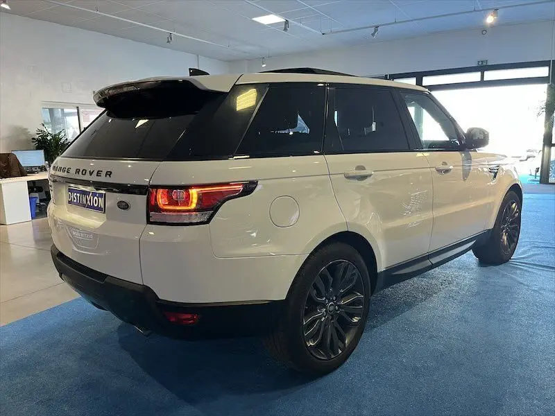 Vue 3/4 arrière droite d'un Range Rover Sport blanc avec jantes noires dans un showroom lumineux.