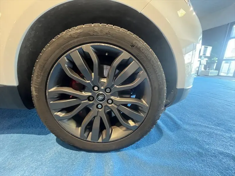 Gros plan sur la roue avant gauche du Range Rover Sport blanc, mettant en valeur la jante alliage sombre au design distinctif.