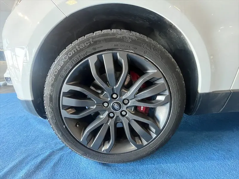 Gros plan sur la roue avant gauche du Range Rover Sport blanc, soulignant l'arc de roue et le pneu tout-terrain.
