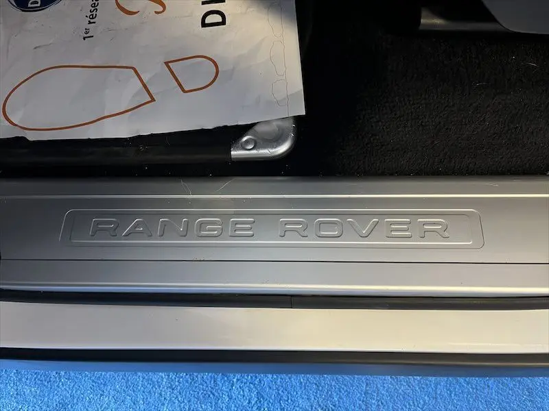 Gros plan sur la plaque de seuil de porte argentée avec l'inscription Range Rover, intérieur noir visible.