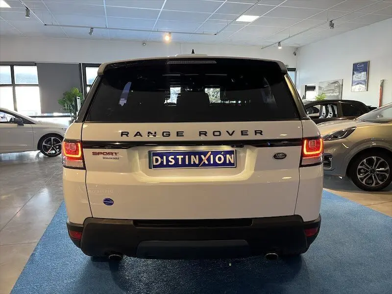 Vue arrière d'un Range Rover Sport blanc 2018 avec feux allumés dans un showroom lumineux