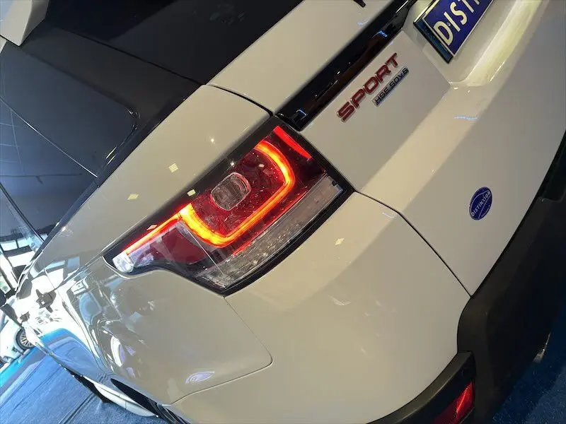 Feu arrière droit allumé d'un Range Rover Sport blanc 2018, vue rapprochée sur l'arrière avec logo et plaques visibles.