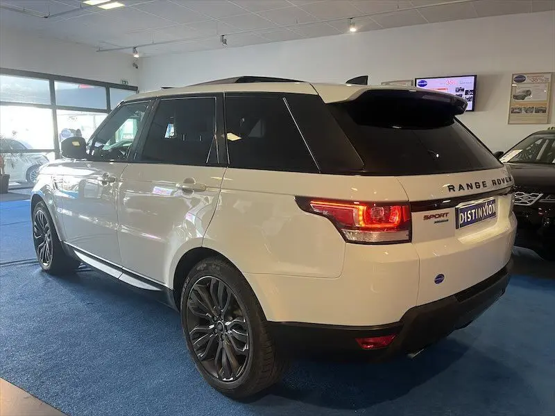 Vue 3/4 arrière droite d'un Range Rover Sport blanc avec jantes noires et feux arrière allumés en showroom.
