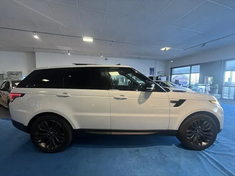 Vue de profil côté gauche d'un Range Rover Sport blanc avec jantes noires dans un showroom lumineux.