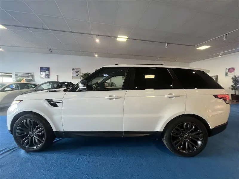 Profil côté gauche d'un Range Rover Sport blanc avec toit noir et jantes noires en concession.