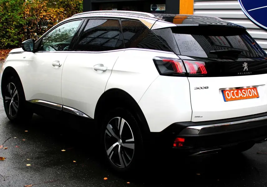 Peugeot 3008 blanc nacré vu de trois quarts arrière droit, toit panoramique noir et feux arrière LED allumés.