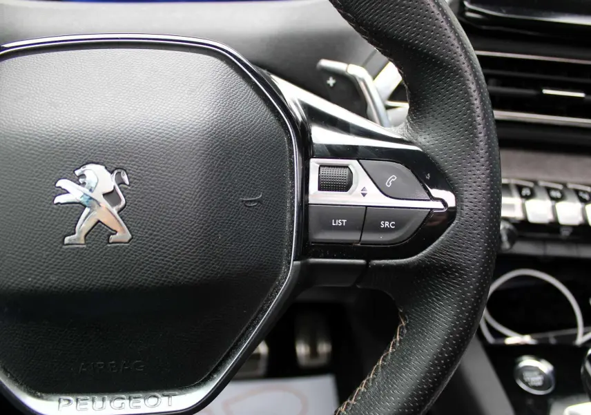 Gros plan sur le volant en cuir perforé noir du Peugeot 3008 2025 avec commandes intégrées et logo lion argenté.