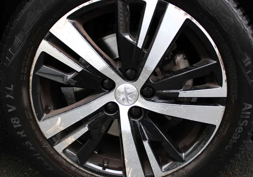 Gros plan sur la jante bi-ton noire et argentée avec logo Peugeot, montée sur un pneu Continental AllSeason.