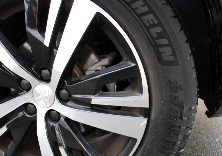 Gros plan sur la jante bi-ton noire et argentée avec logo Peugeot, montée d'un pneu Michelin sur un véhicule blanc nacré.