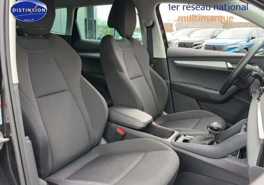 Vue intérieure côté avant droit du Skoda Karoq noir 2025, montrant sièges tissu gris et accoudoir central.