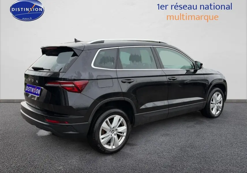 Vue 3/4 arrière droite d'un Skoda Karoq noir avec jantes alu et barres de toit sur fond neutre.