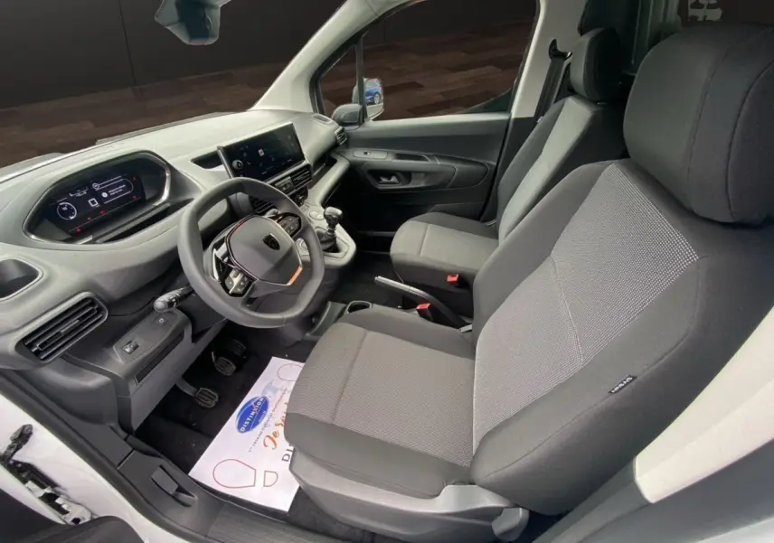 Vue intérieure côté conducteur du Peugeot Partner blanc 2024, montrant le tableau de bord numérique et les sièges gris.