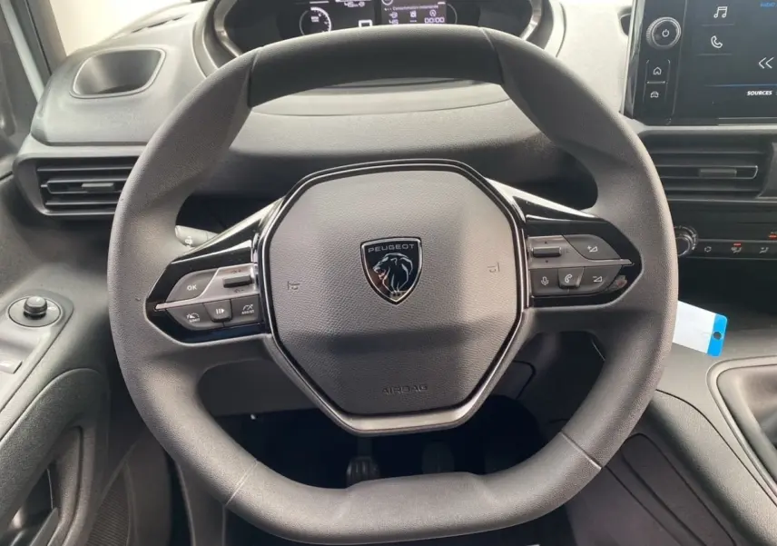 Vue rapprochée du volant multifonctions Peugeot noir dans l’habitacle du Partner 2024 avec tableau de bord et écran tactile.