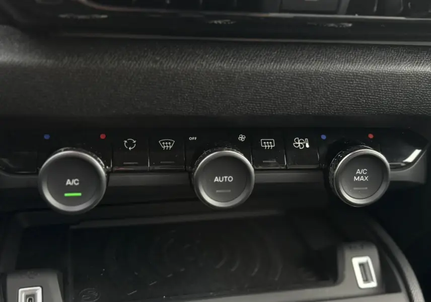 Gros plan sur la console centrale noire du Citroën C4 Hybrid 2025 avec commandes de climatisation et recharge sans fil.