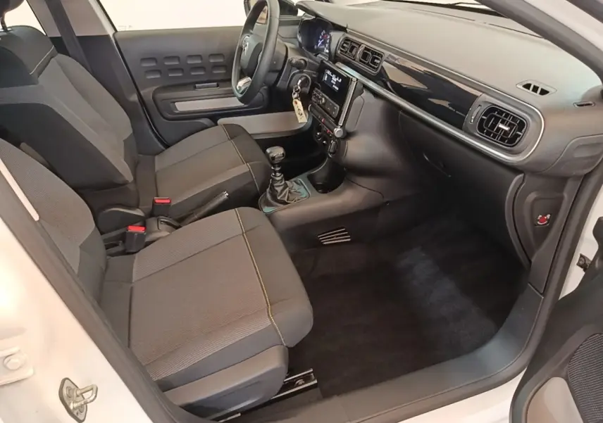 Vue intérieure côté conducteur de la Citroën C3 blanche, montrant sièges gris, volant multifonctions et tableau de bord moderne.