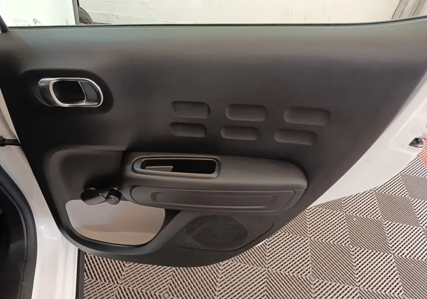 Vue intérieure du panneau de porte avant gauche noir de la Citroën C3 blanche de 2019, avec poignée et haut-parleur intégrés.