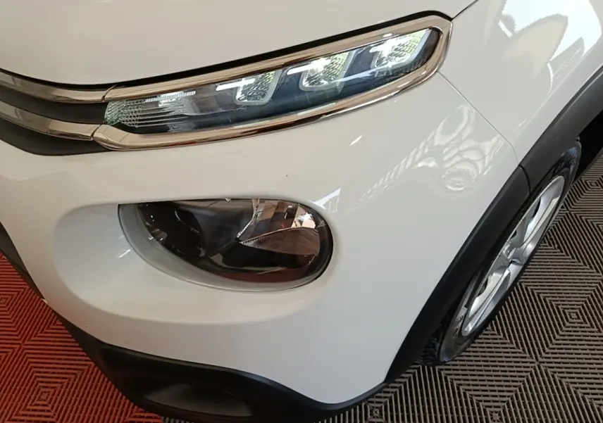Gros plan sur l'avant droit blanc d'une Citroën C3 2019, mettant en valeur ses phares distinctifs et la roue.