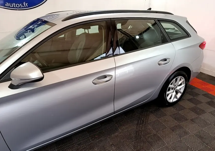 Vue latérale gauche d'une SEAT Leon gris clair en intérieur, mettant en valeur ses lignes fluides et ses jantes alliage.