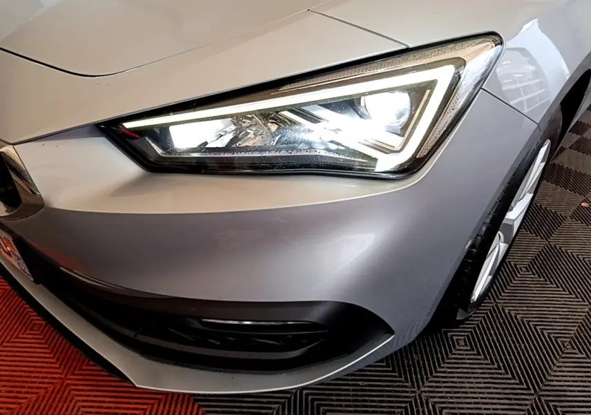 Gros plan sur le phare avant droit allumé d'une SEAT Leon gris foncé, avec partie de la roue visible.