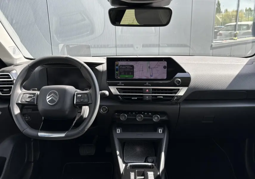 Vue intérieure avant du tableau de bord et volant noir du Citroën C4 Hybrid 2025 avec écran tactile GPS et commandes au volant.