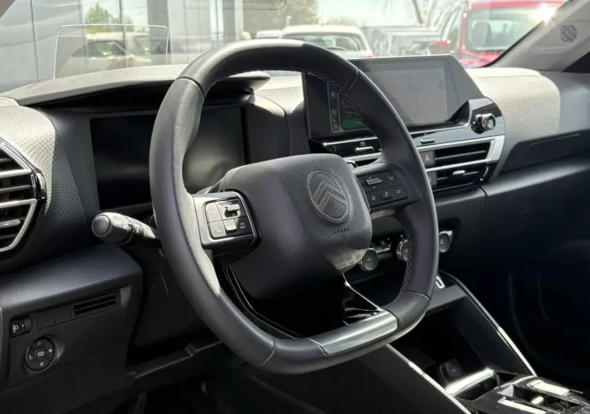 Vue intérieure centrée sur le volant cuir du Citroën C4 Hybrid 2025 avec écran tactile et tableau de bord noir.