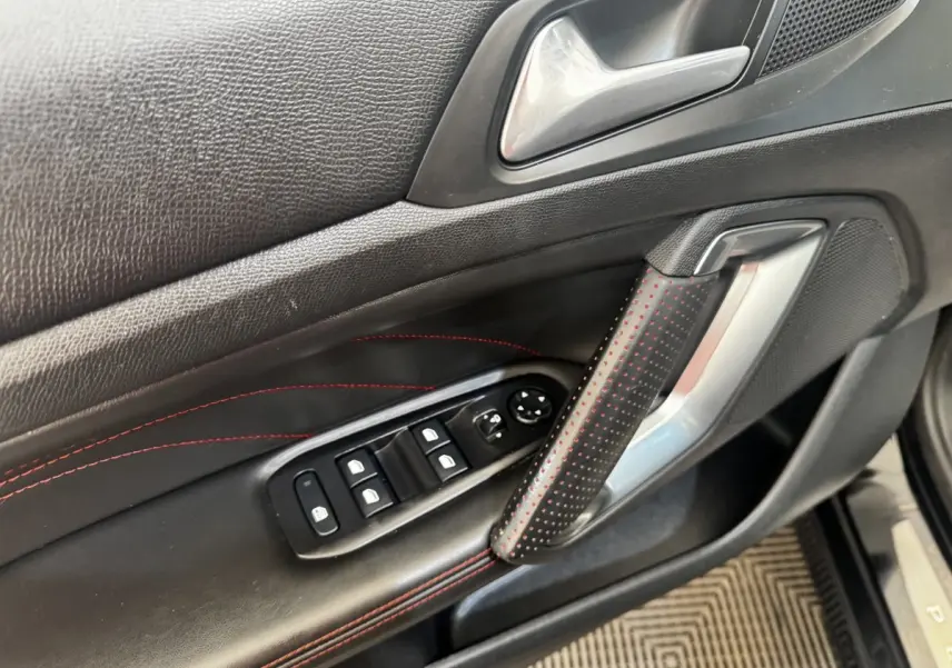 Gros plan sur la porte intérieure côté conducteur de la Peugeot 308 noire, avec surpiqûres rouges et commandes des vitres.