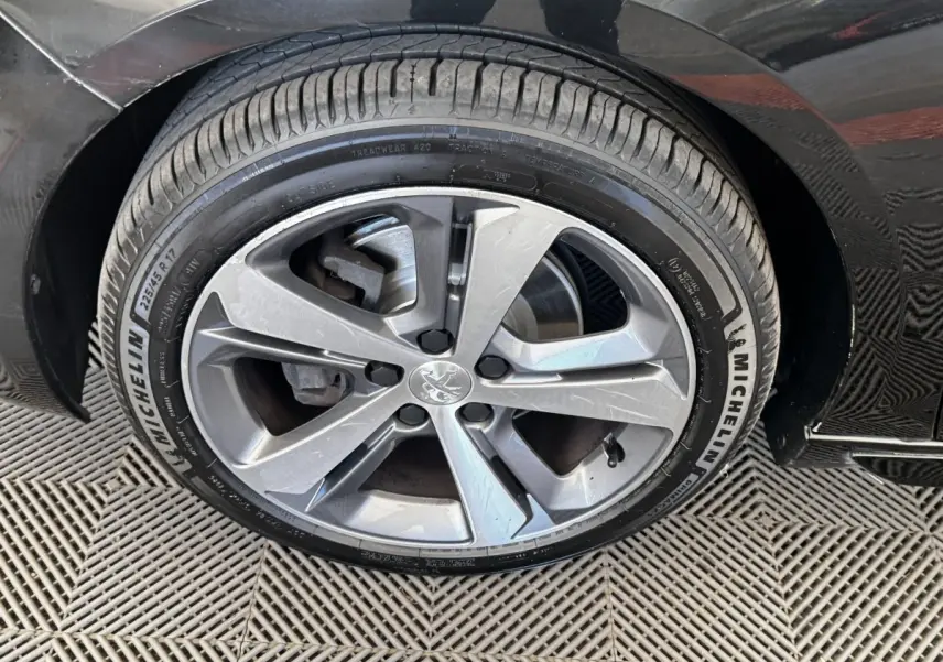 Gros plan sur la roue avant droite de la Peugeot 308 noire, jante alliage à cinq branches doubles, pneu Michelin.