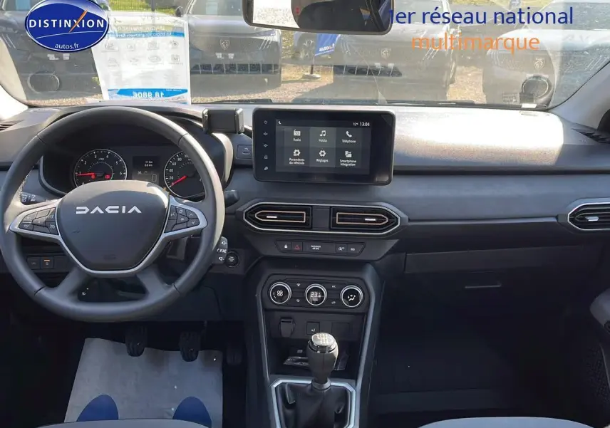 Vue intérieure avant du tableau de bord et volant DACIA Sandero 2025 avec écran tactile et levier de vitesses manuel.