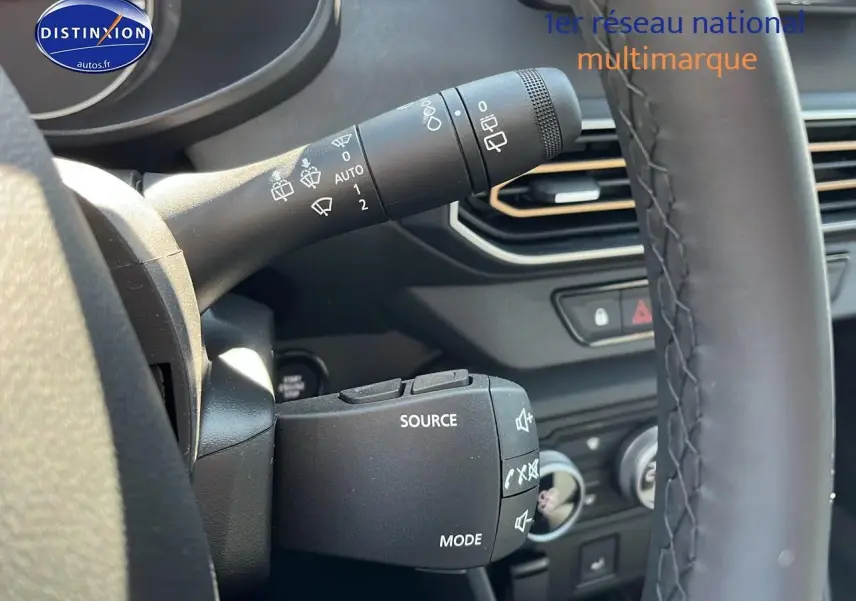 Gros plan sur les commandes au volant et manette d'essuie-glace d'une Dacia Sandero 2025 vert cèdre, intérieur noir.