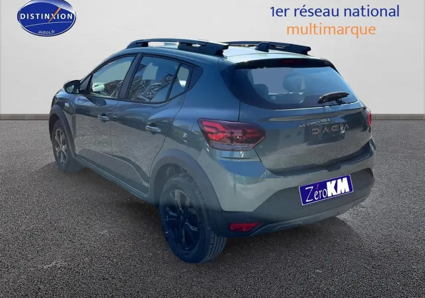 Vue 3/4 arrière droite d'une Dacia Sandero 2025 vert cèdre avec jantes alu et barres de toit visibles.