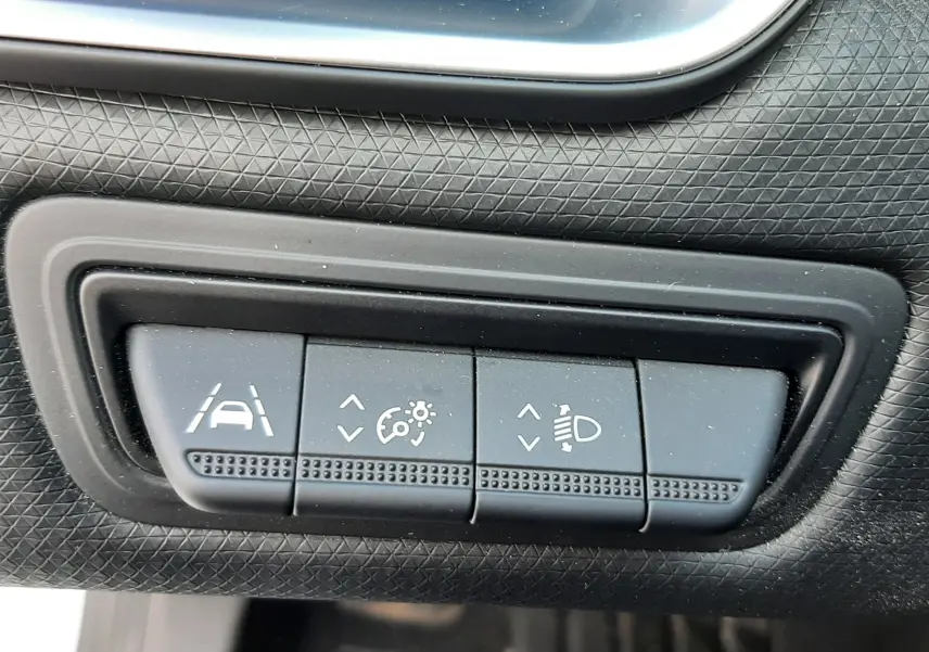 Gros plan sur les boutons de réglage d'assistance et éclairage du tableau de bord d'une Renault Clio V blanche.