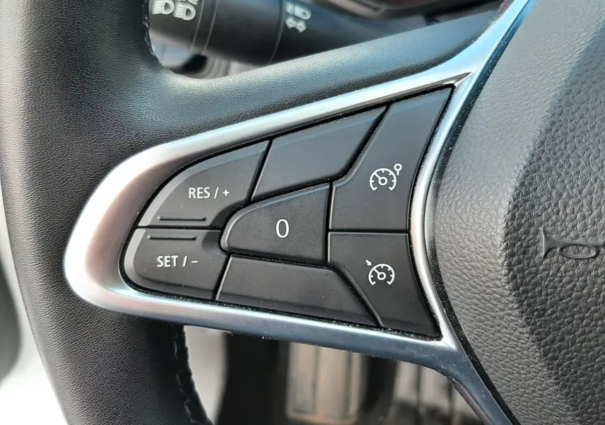 Gros plan sur les commandes de régulateur de vitesse à gauche du volant noir d'une Renault Clio V blanche de 2022.