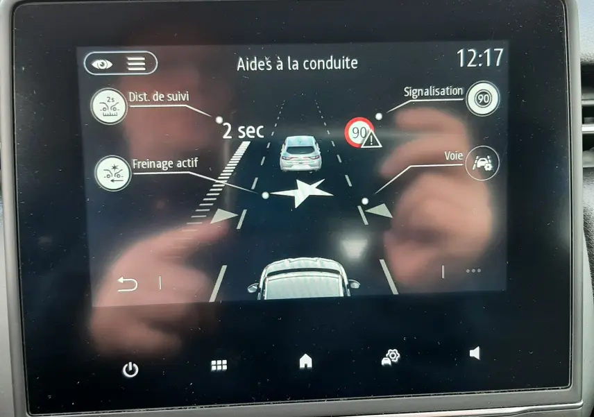 Écran tactile intérieur de la Renault Clio V blanc montrant les aides à la conduite avec distance de suivi et signalisation.