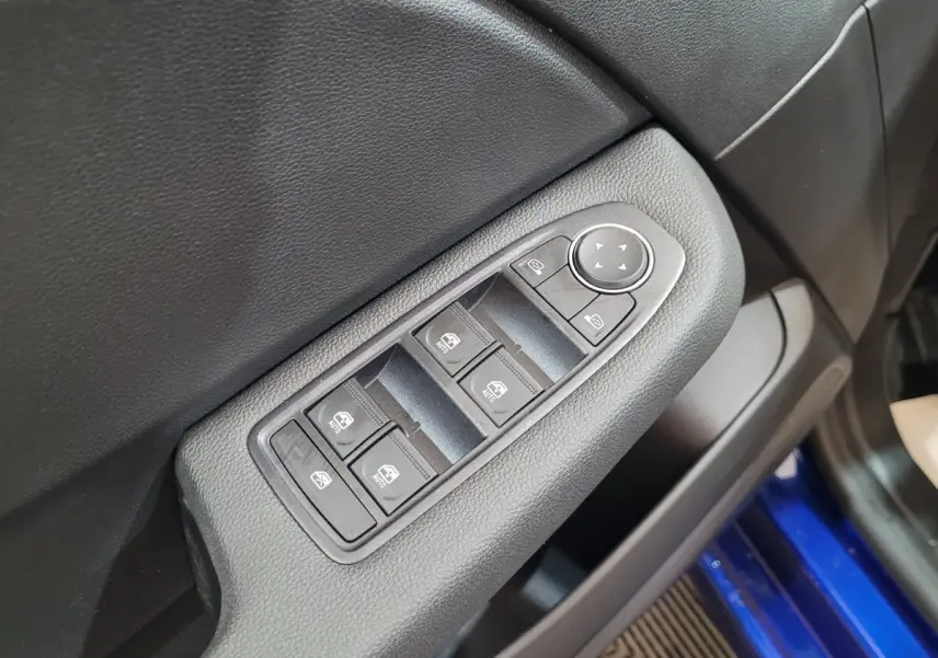 Gros plan sur les commandes des vitres électriques côté conducteur d’une Renault Clio bleu 2025, intérieur noir.