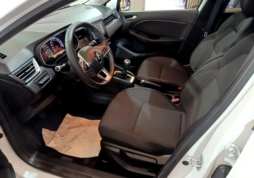 Vue intérieure côté conducteur de la Renault Clio Business blanche, montrant le volant cuir et la console avec boîte manuelle.