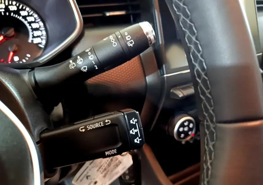 Gros plan sur les commandes au volant côté gauche d’une Renault Clio Business blanche, avec tableau de bord partiellement visible.