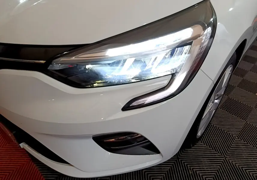 Gros plan sur l'avant droit blanc d'une Renault Clio 2021 avec phares LED allumés et jante visible.