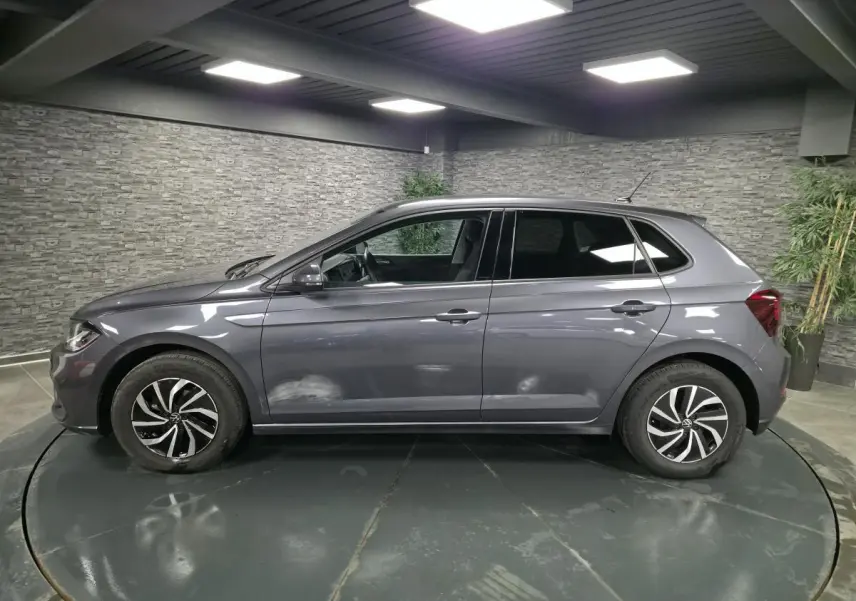 Profil côté gauche d'une Volkswagen Polo gris métallisé 2025 avec jantes alliage et vitres arrière surteintées dans un showroom.