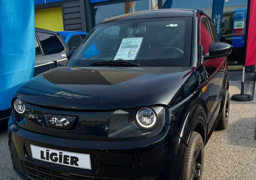 Vue 3/4 avant d'une Ligier Myli I.DEL 8KWH noire intense électrique, devant un magasin Ligier Store.