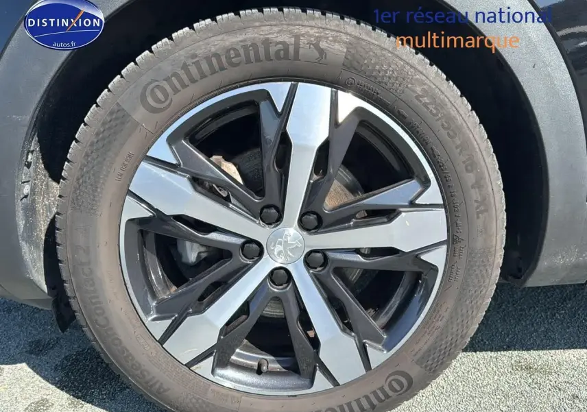 Gros plan sur la jante alu bi-ton noire et argent avec logo Peugeot sur un Peugeot 3008 noir métal.
