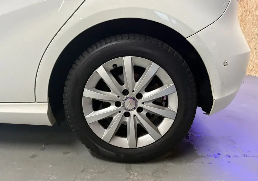 Gros plan sur la roue arrière droite blanche d'une Mercedes Classe A 200D 2016 avec jante argentée et logo Mercedes visible.