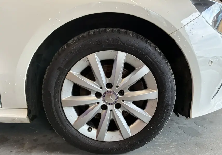 Gros plan sur la roue avant gauche d'une Mercedes Classe A 200D blanche avec jante alliage et logo central visible.