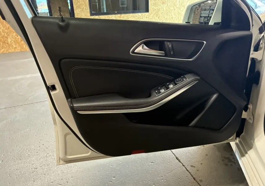Vue rapprochée de la porte avant gauche ouverte d'une Mercedes Classe A 200D blanche, intérieur noir avec commandes électriques.
