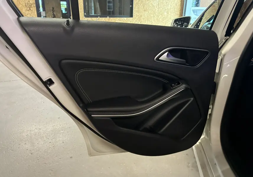 Vue rapprochée de la porte arrière gauche blanche d'une Mercedes Classe A 200D avec garniture intérieure noire et surpiqûres blanches.
