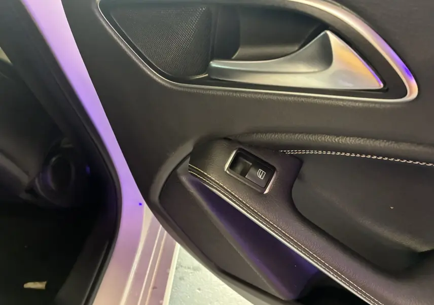 Gros plan sur la portière intérieure côté gauche d'une Mercedes Classe A 200D blanche, avec garniture cuir noire et commande de vitre.