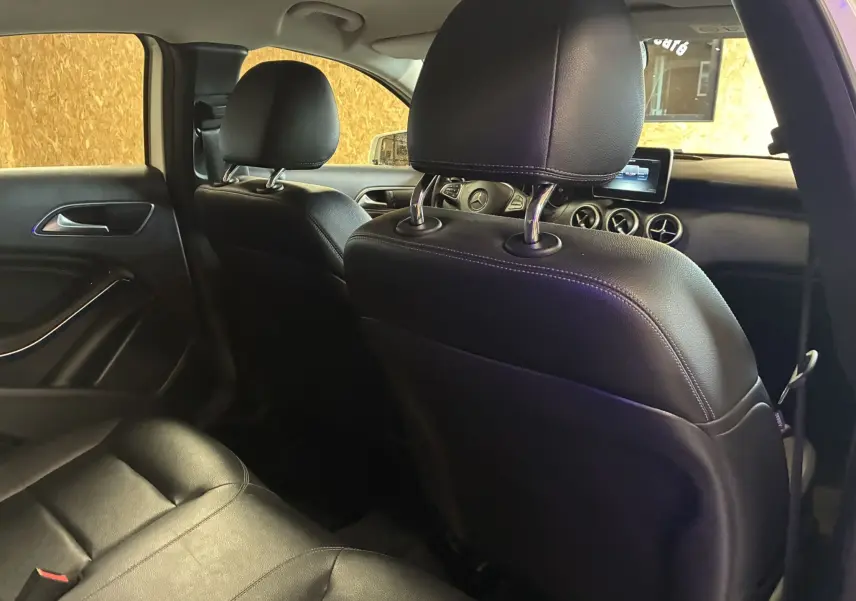Intérieur noir cuir d'une Mercedes Classe A 200D 2016 vu depuis l'arrière côté gauche, avec tableau de bord et écran visible.